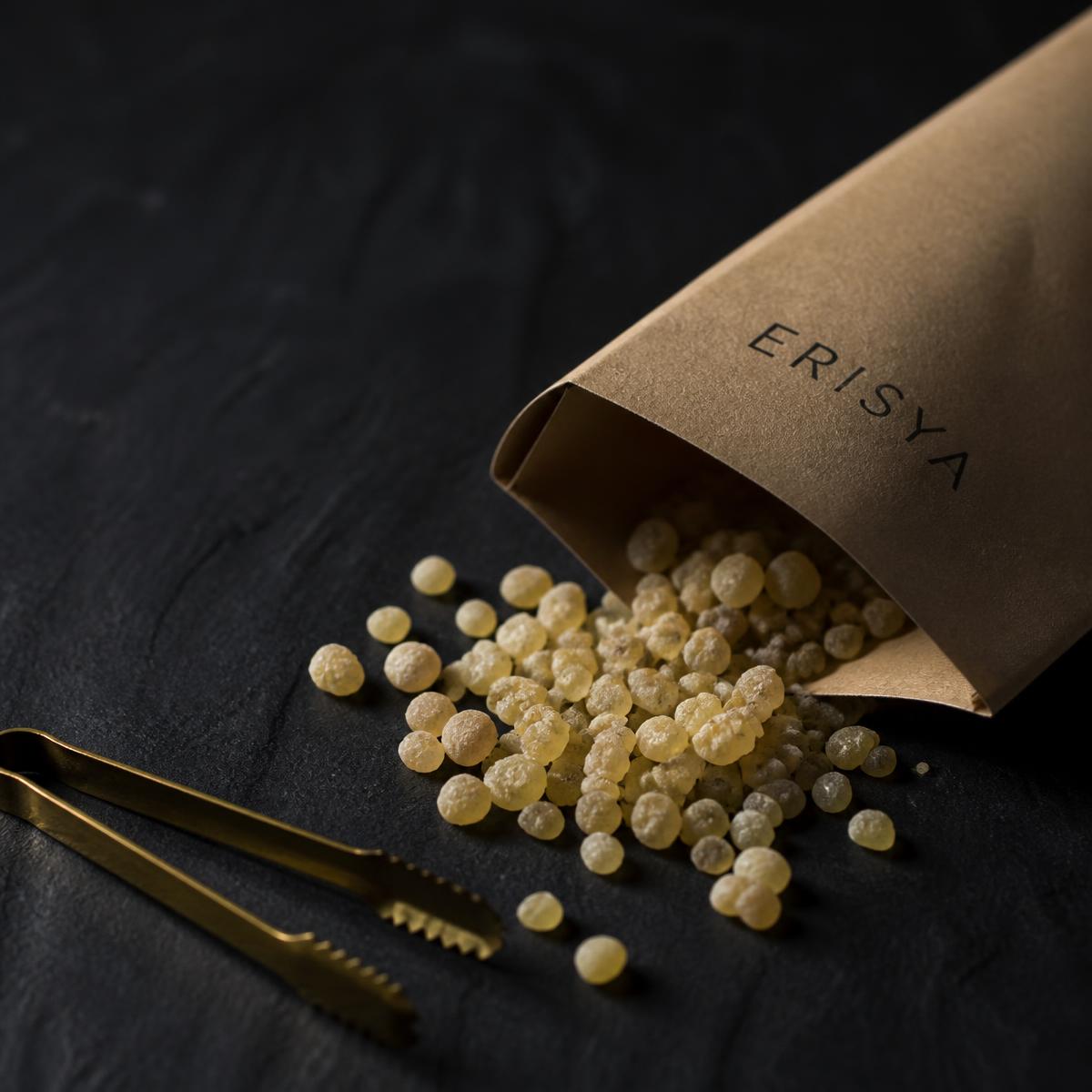 Larmes d'oliban Shazri, tri omanais au calibre plus petit, versées d'un sachet kraft ERISYA sur une ardoise sombre.
